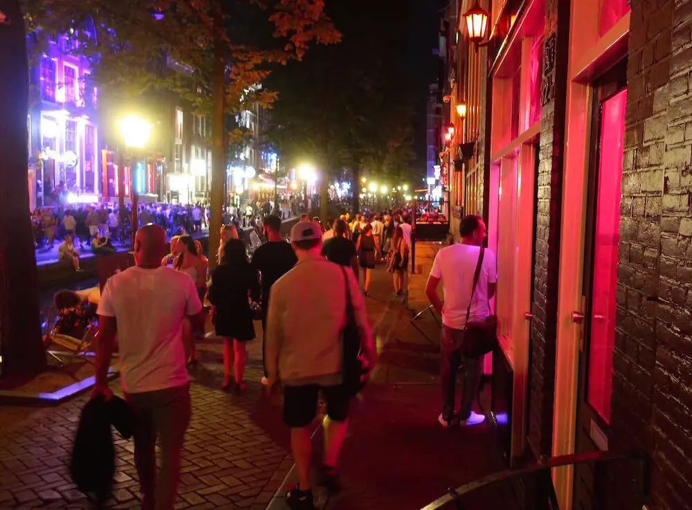 Oudezijds Achterburgwal at night in Amsterdam red light district with tourists on the street and a man talking to a window prostitute