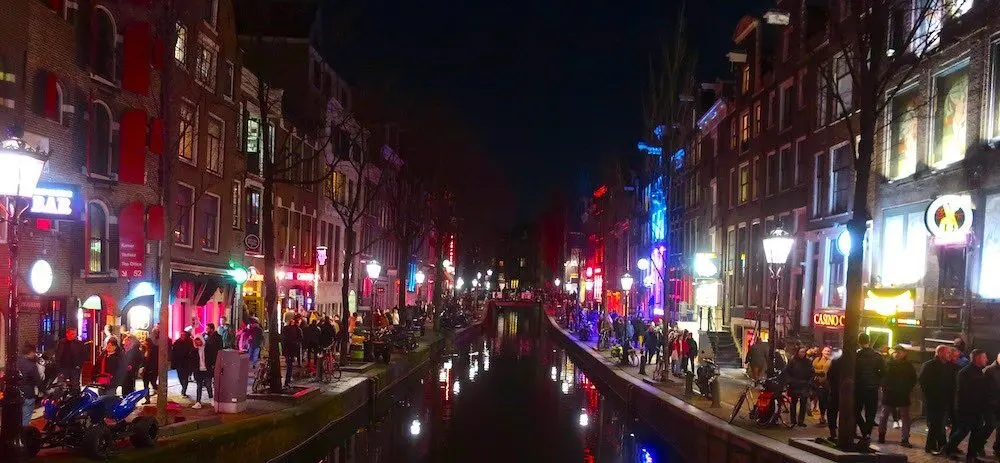 Oudezijds Achterburgwal bij nacht met toeristen op straat in de Wallen van Amsterdam