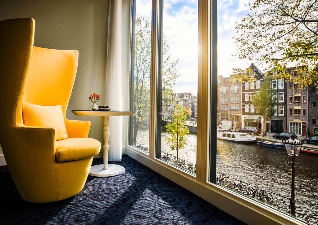 Hotelzimmer mit einem gelben Stuhl mit Blick auf eine Amsterdamer Gracht