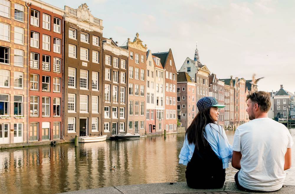 a young couple in Amsterdam with the old Dutch houses and a canal in the back