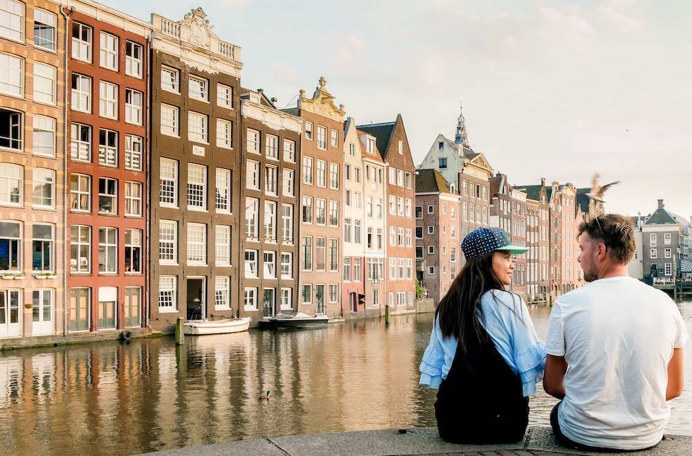 ein junges Paar in Amsterdam mit den alten holländischen Häusern und einer Gracht im Hintergrund