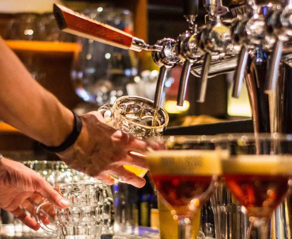 barman taps a big glass of beer while holding another empty beer glass 