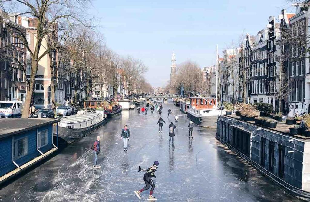 Frozen canal in Amsterdam and people ice skating in winter clothing 