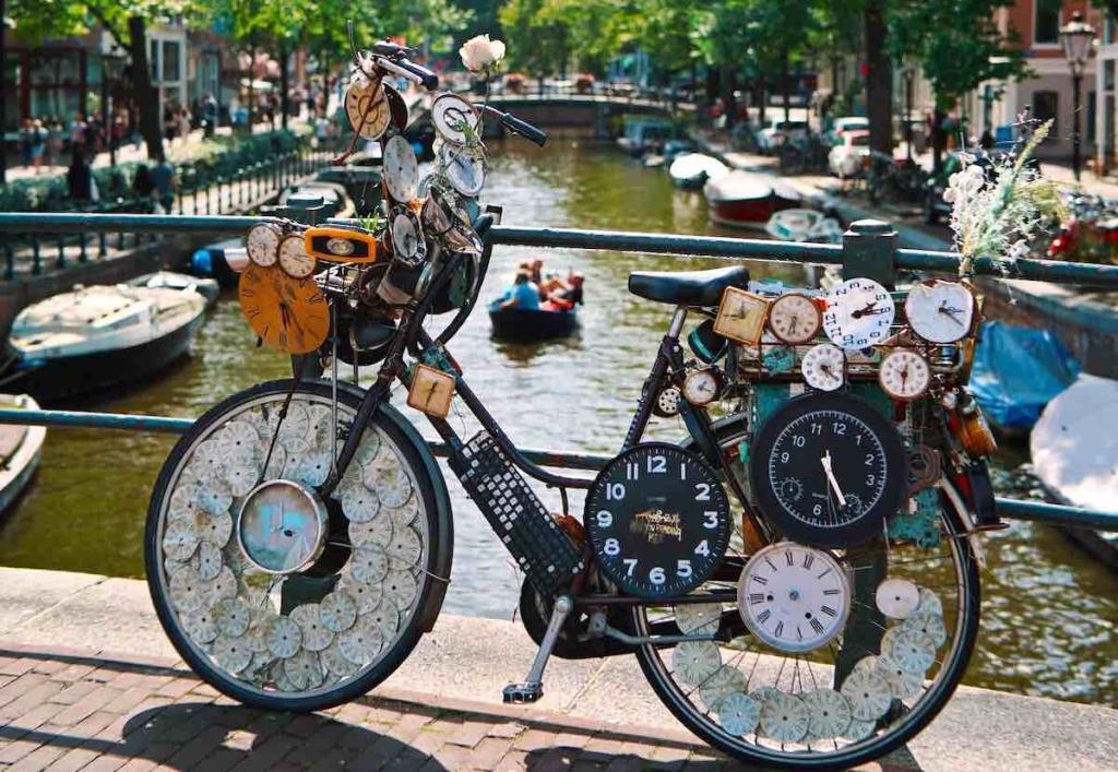 bicycle with dozens of clocks on an Amsterdam canal during a sunny day and boats on the background