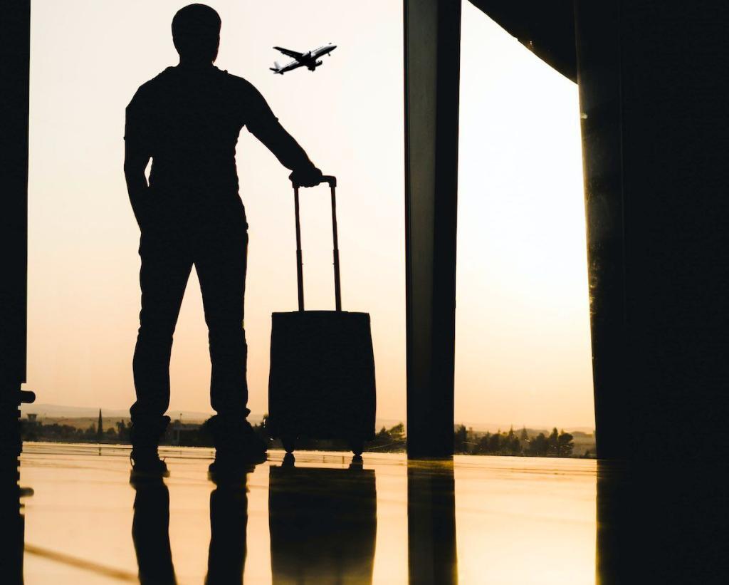 man with suitcase waiting on airport while watching a plane depart.