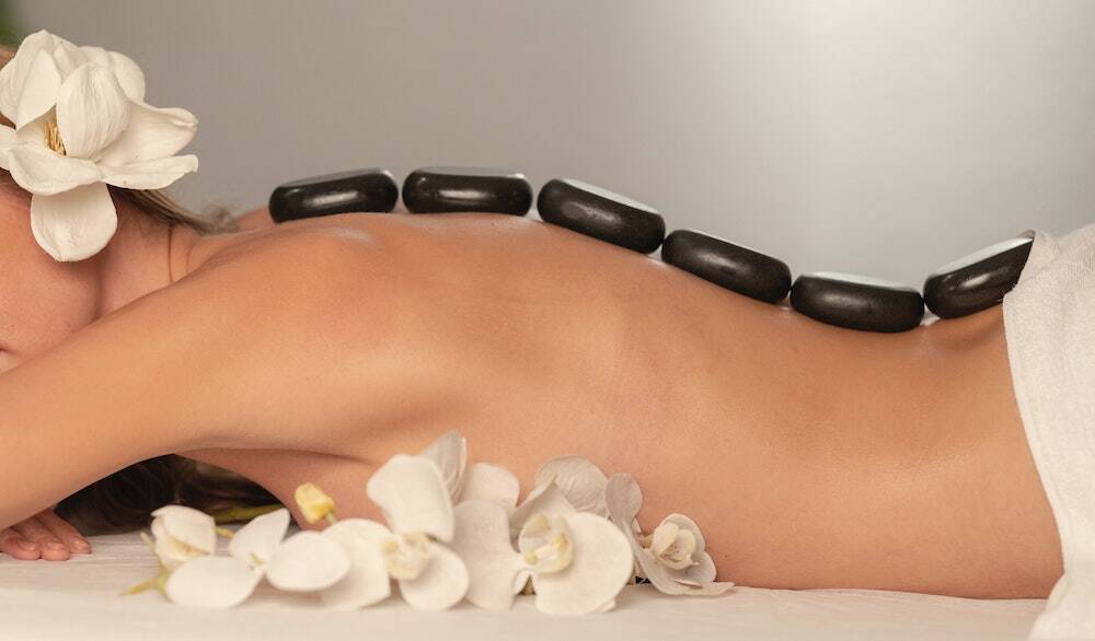 black hot stones are placed on the back of woman on a bed
